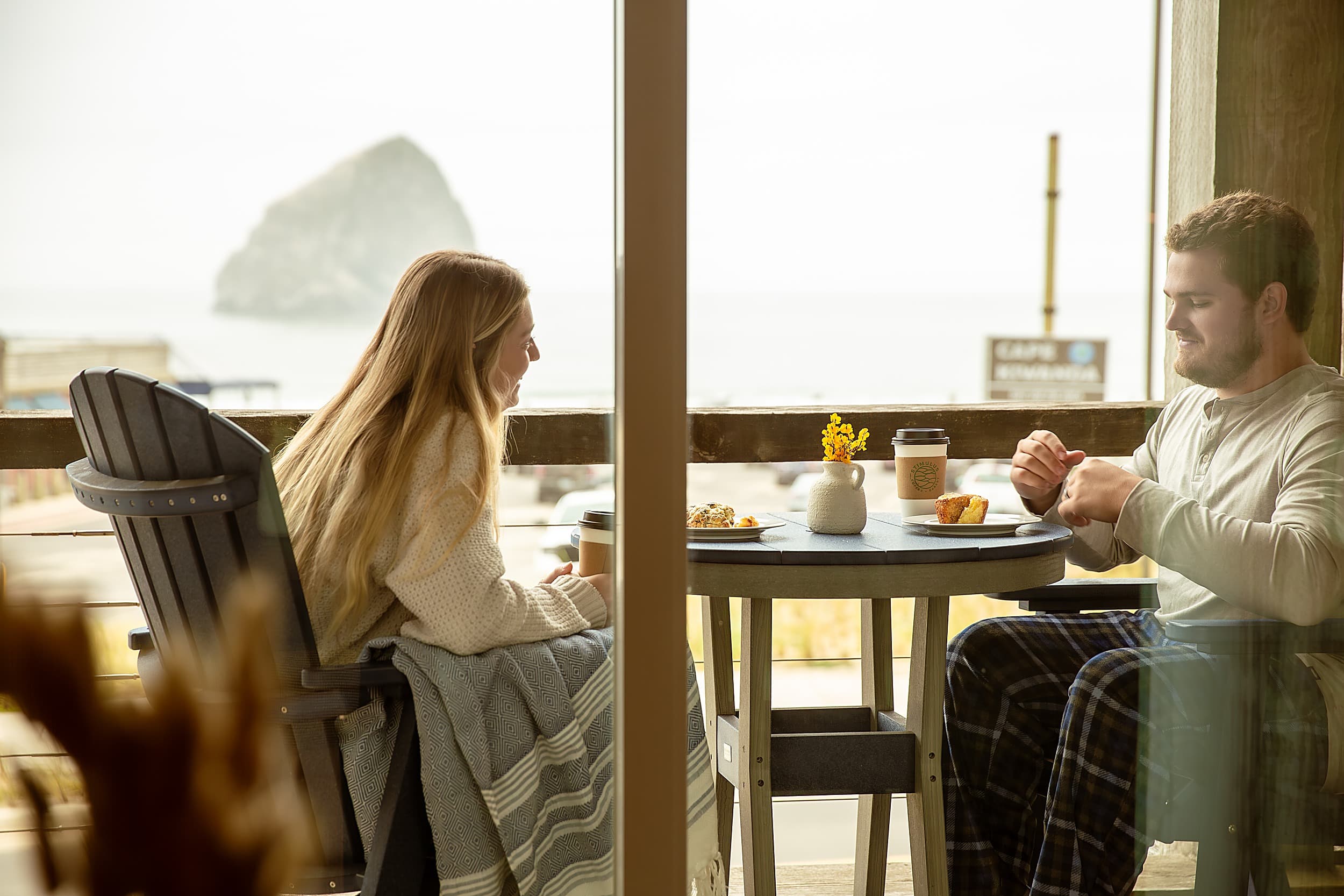 Couple shares coffee and pastries on a private balcony overlooking Haystack Rock at the Inn at Cape Kiwanda, an oceanfront hotel in Pacific City, Oregon.