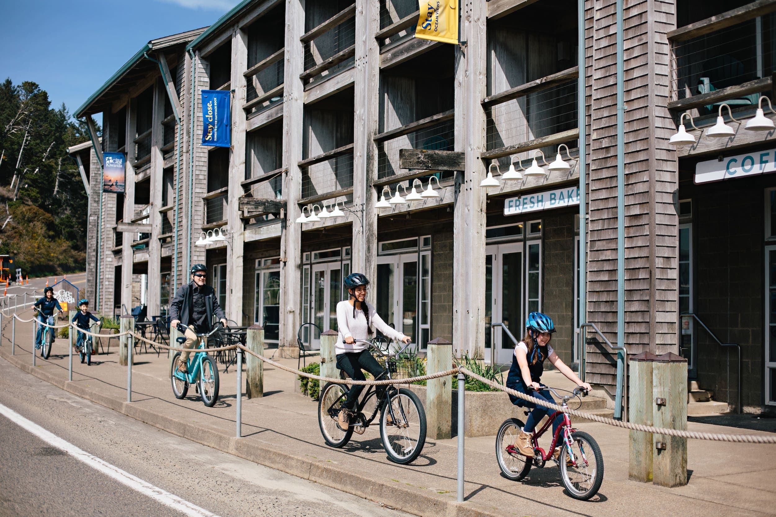 A family biking on the sidewalk in front of a coffee shop near Inn at Cape Kiwanda