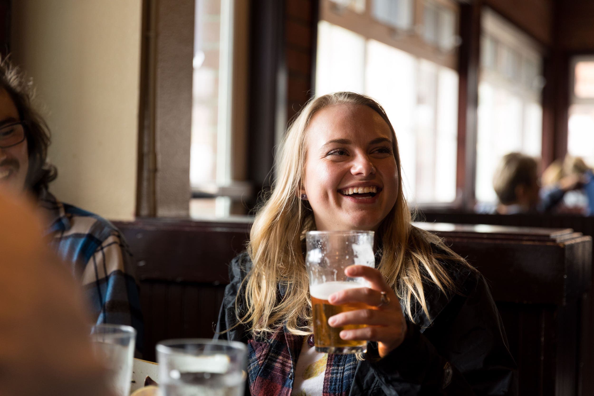 A woman smiling while drinking a beer at Pelican Bar & Brewery