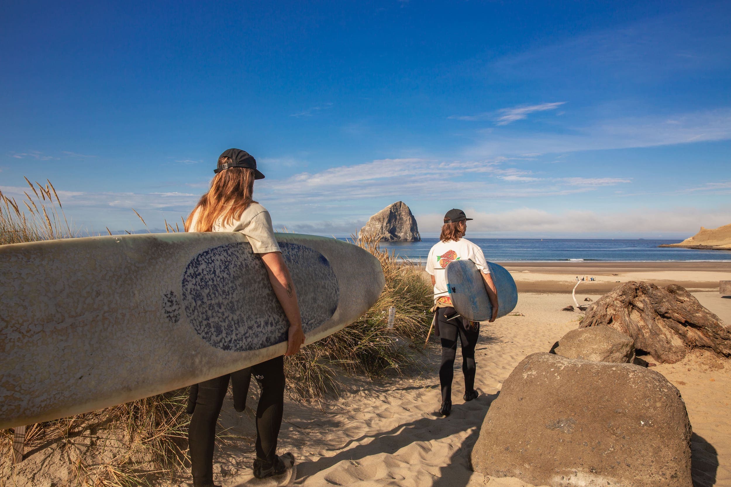 Two people walking on the beach, each with surf boards near Inn at Cape Kiwanda