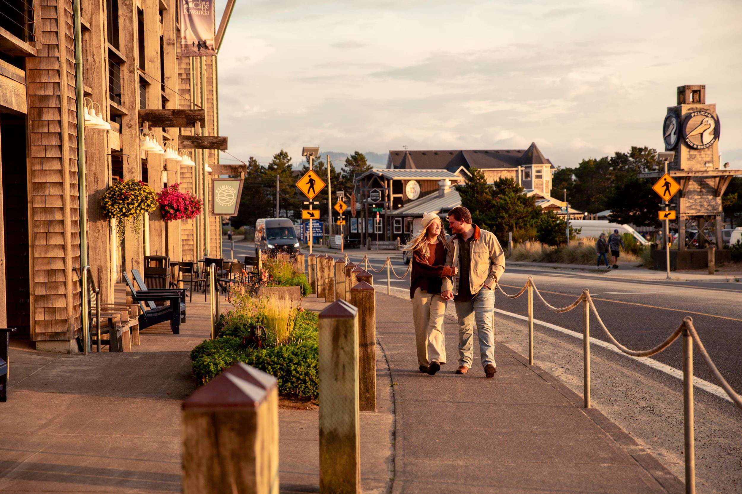 A couple walking down the sidewalk in front of Stimulus Coffee and Pelican Pub & Brewery at In at Cape Kiwanda