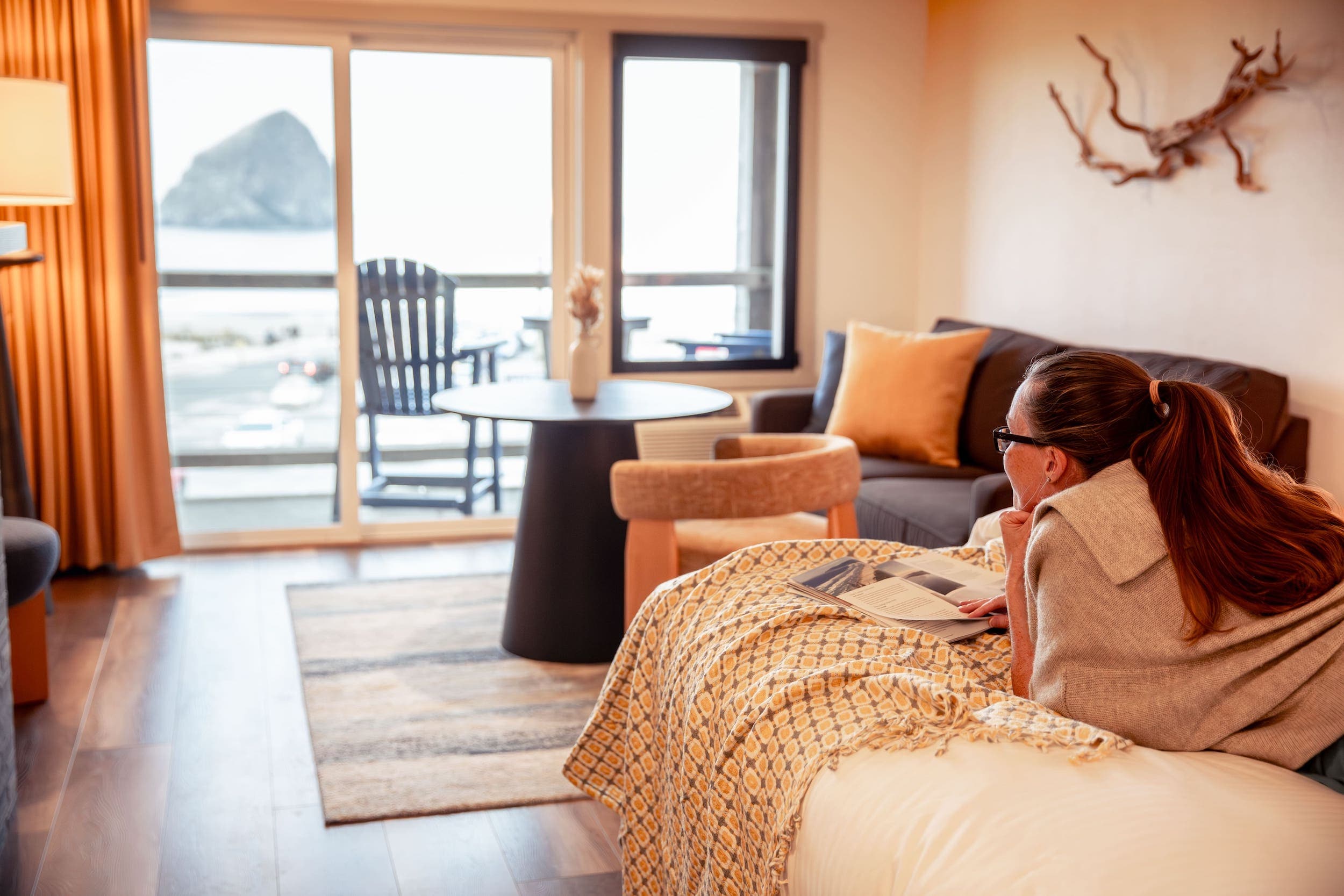 A lady laying on a bed in her room reading a magazine at Inn at Cape Kiwanda