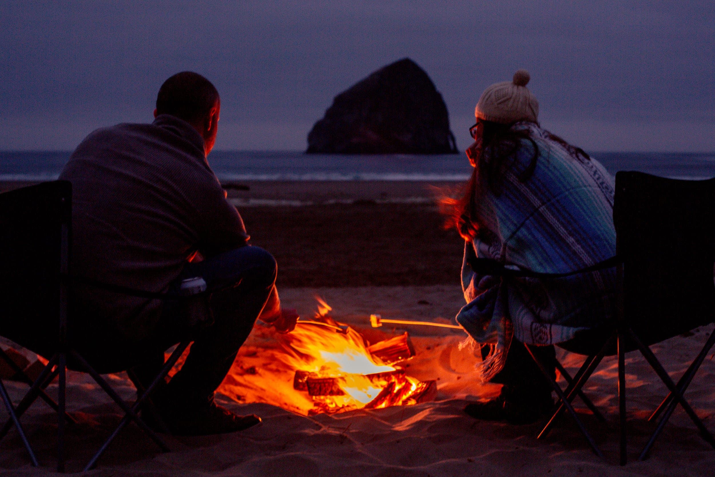 A couple roasting marshmallows in a campfire on the beach at Inn at Cape Kiwanda