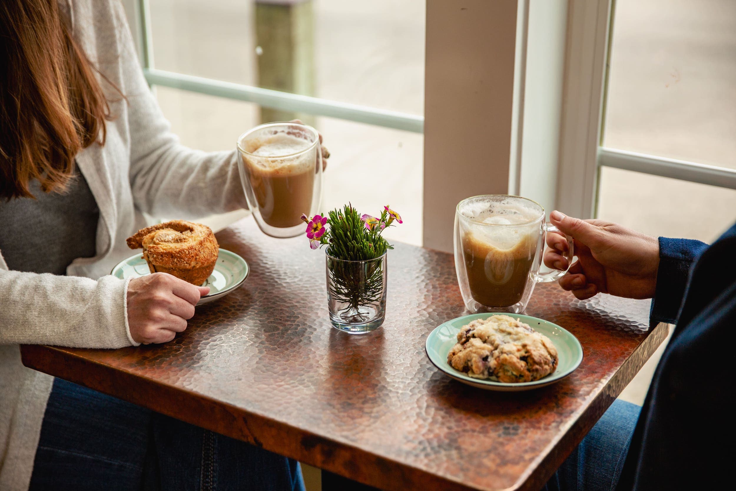 Two people sitting at a table in Stimulus Coffee having hot beverages and baked snacks
