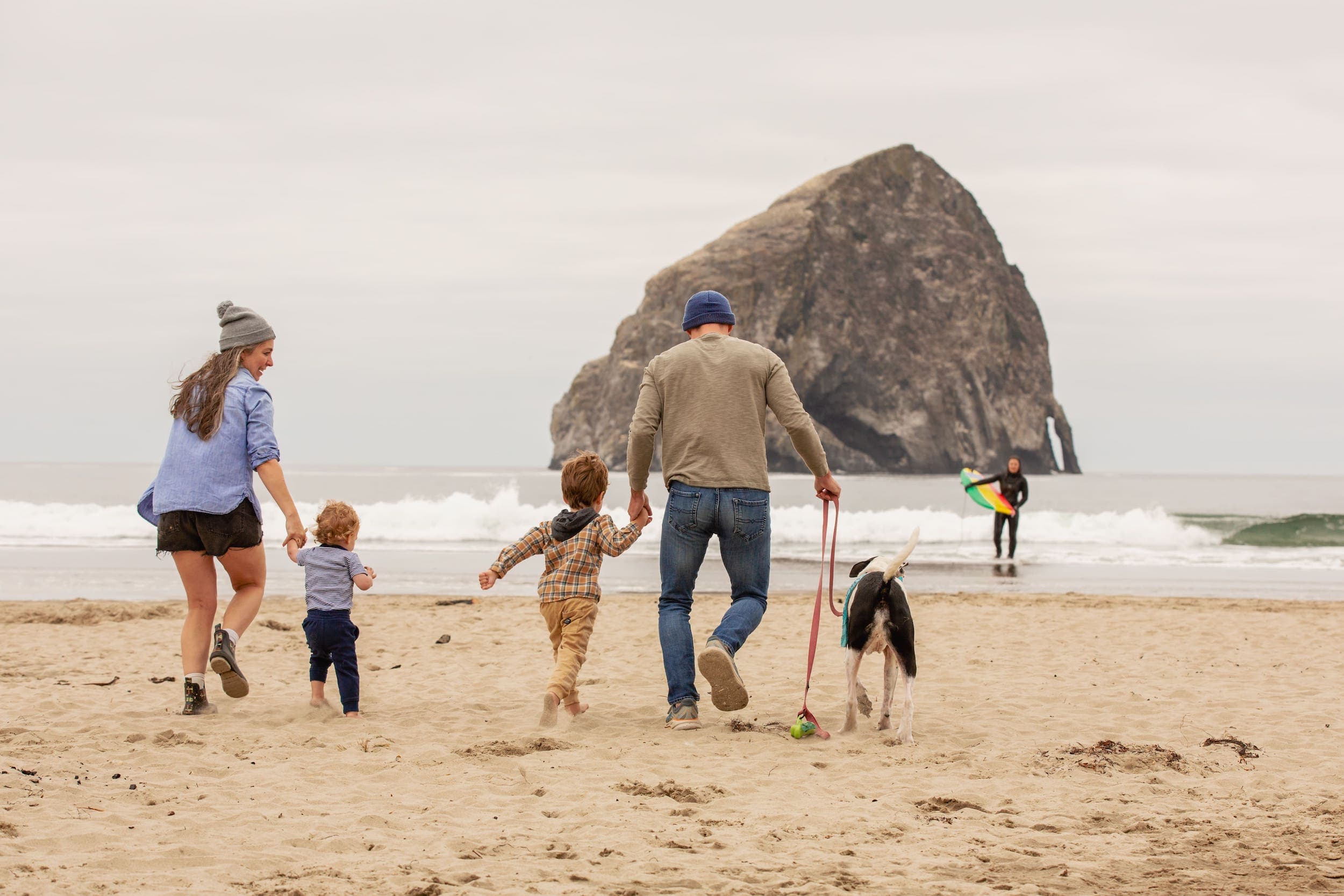 A family walking on the beach and a surfer near Inn at Cape Kiwanda