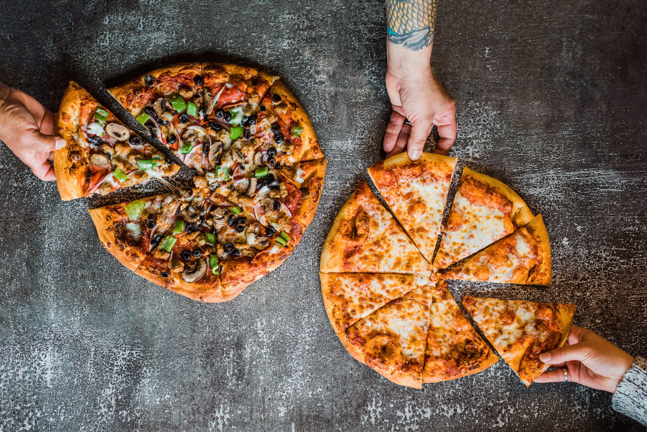 3 hands each taking a slice of a Doryland Pizza pie