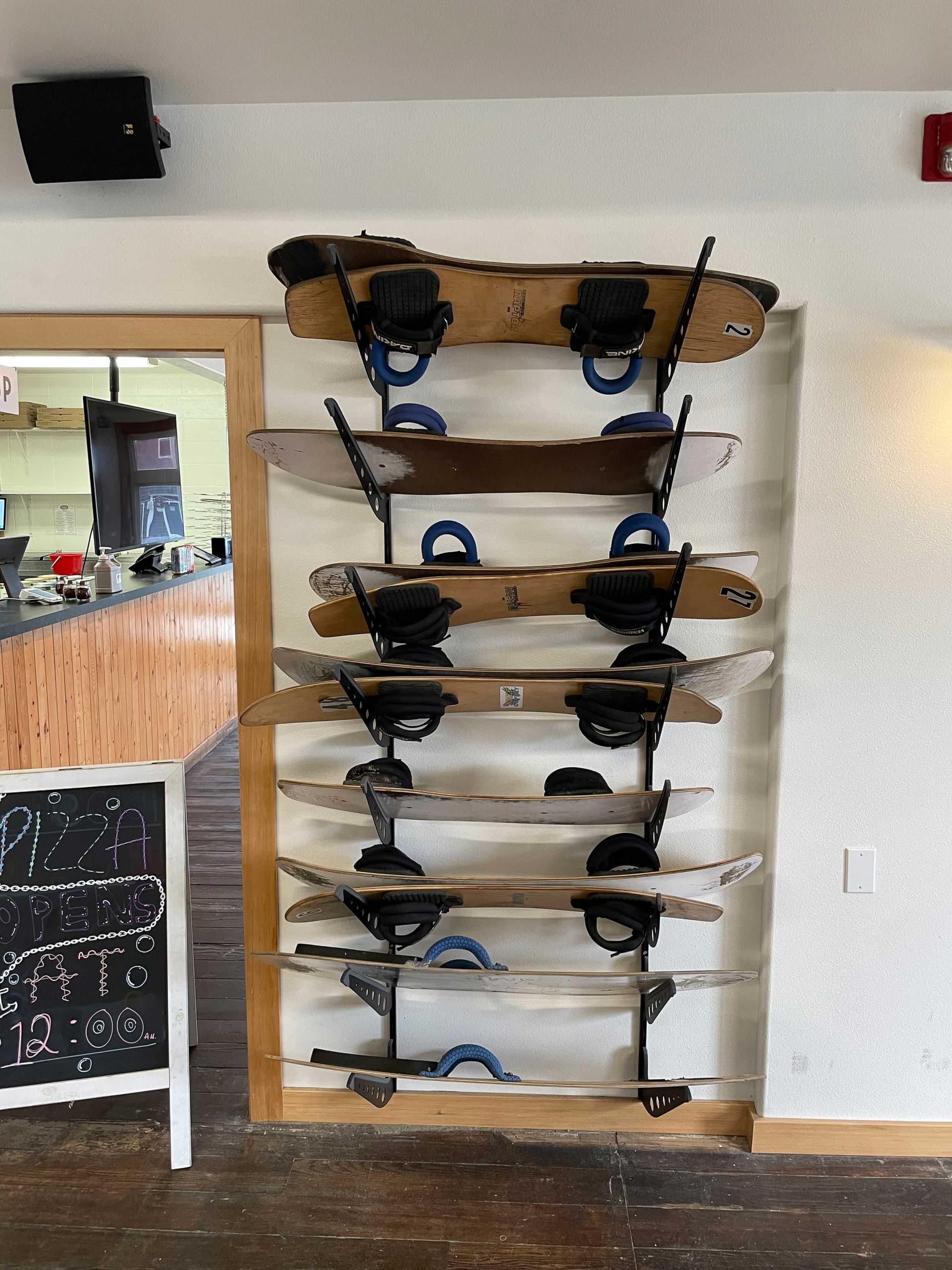 A vertical rack holds six dirt boards with blue bindings against a white wall. A chalkboard sign on the left hints it's inside a rustic café.