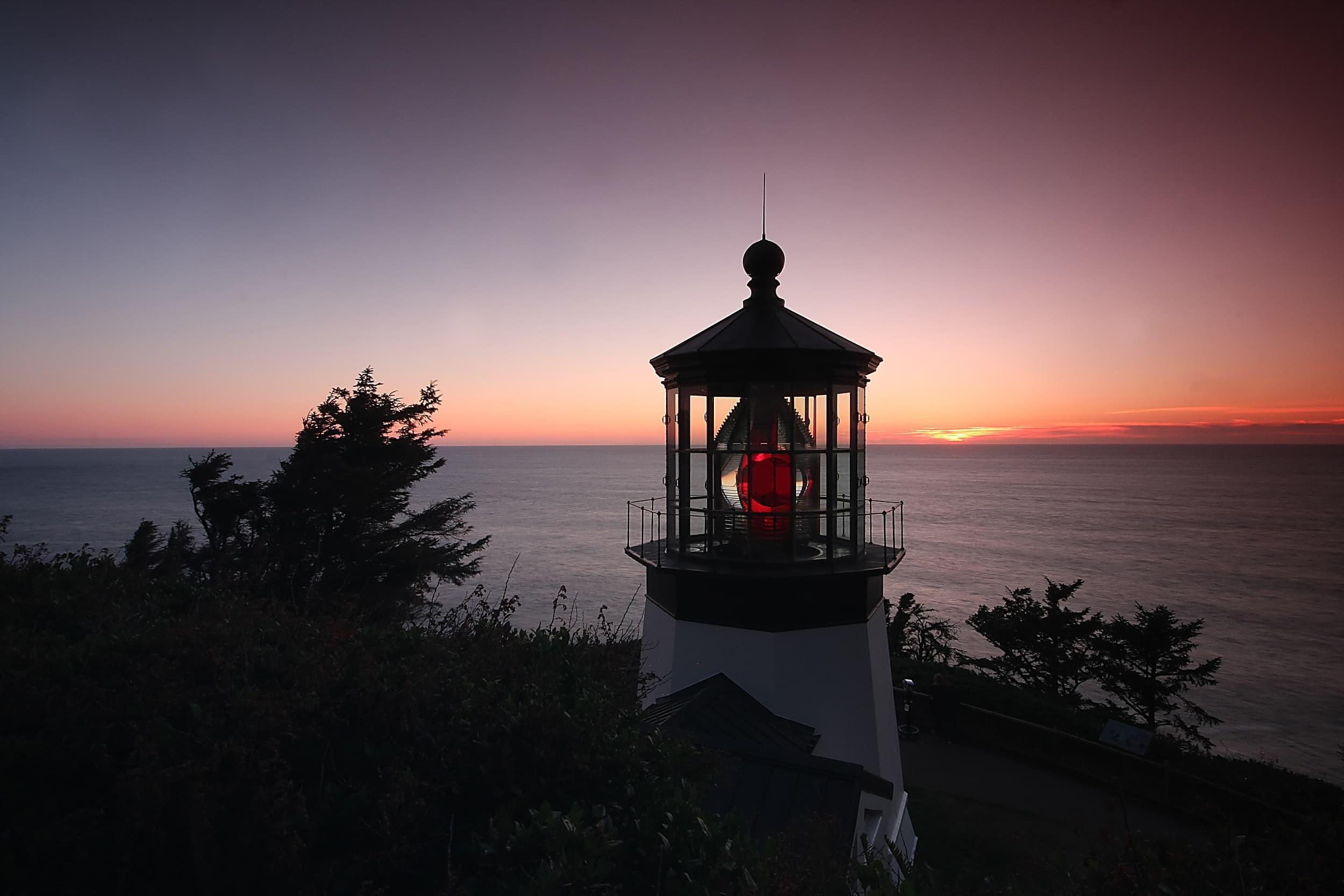 Cape Meares Lighthouse glowing red at sunset over the Pacific Ocean, a scenic day trip from the Inn at Cape Kiwanda in Oregon