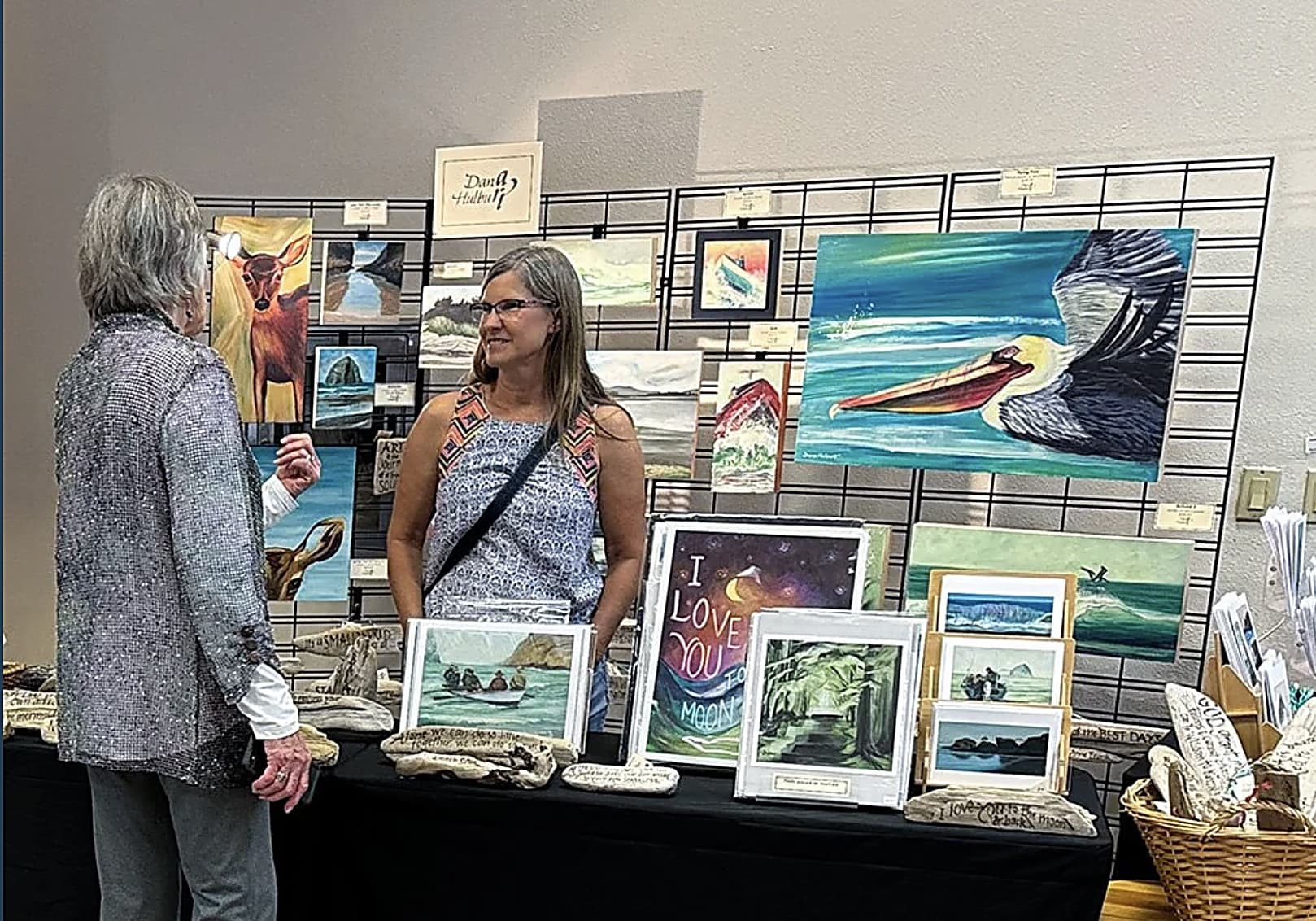 Visitors view colorful ocean and seascape paintings at Nestucca Valley Artisans art festival, Inn at Cape Kiwanda, Pacific City, Oregon Coast